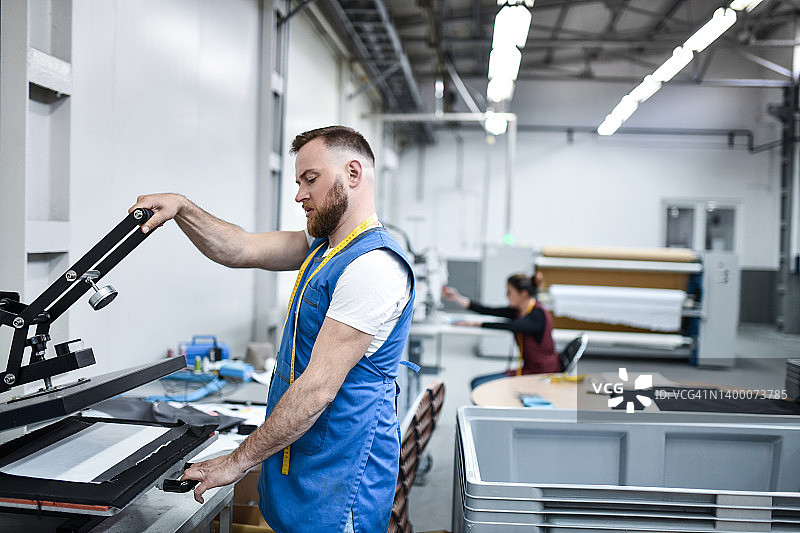 在纺织厂使用布料打印机的络腮胡工人图片素材