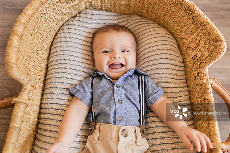 一个22周大的男婴穿着蓝色背带裤套装，躺在海草摩西篮里舒适的奶油色条纹棉毯上图片素材