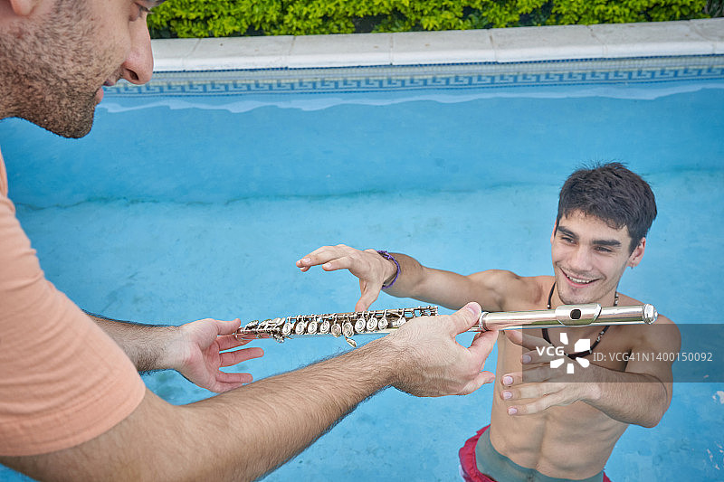 朋友在水池边将长笛递给音乐家图片素材