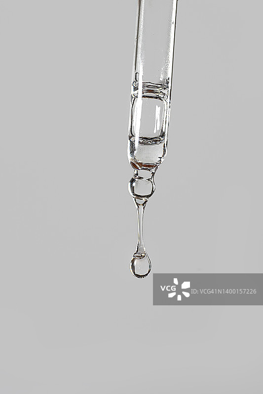 面部精华或精油的滴管特写，带有氧气气泡，滴在粉灰色背景上图片素材