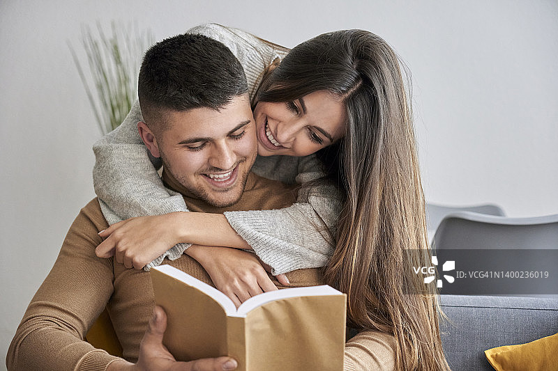 女人在家拥抱正在看书的男友。图片素材