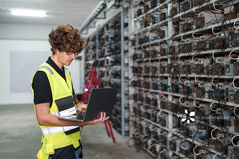 专业工程师携带笔记本电脑在加密货币矿场工作图片素材