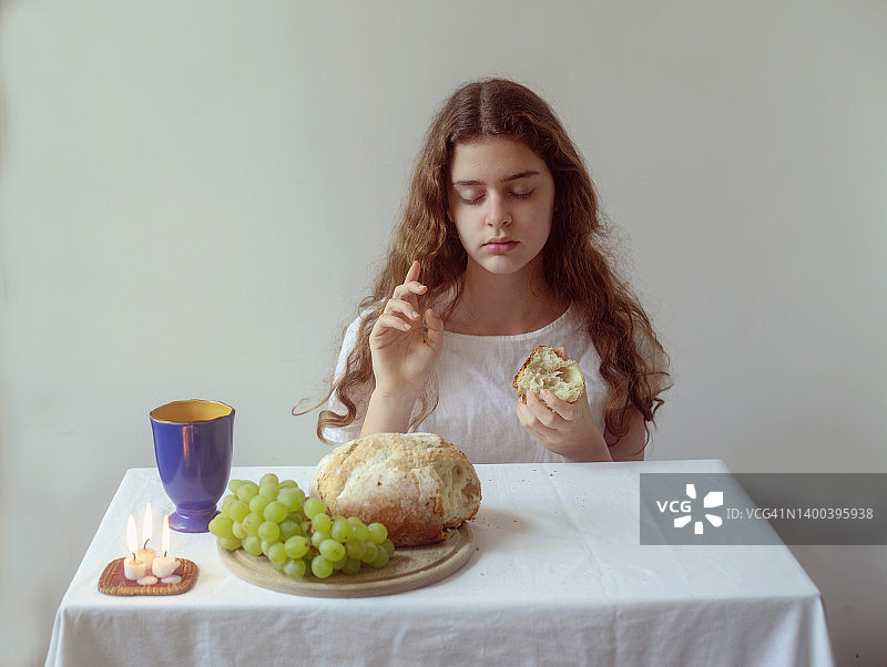 少女坐在摆有面包、葡萄、蜡烛和玻璃杯的桌子前图片素材