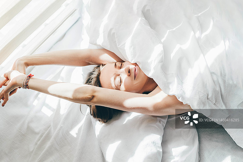 阳光明媚的早晨，女子在被子下睡觉（俯视）图片素材