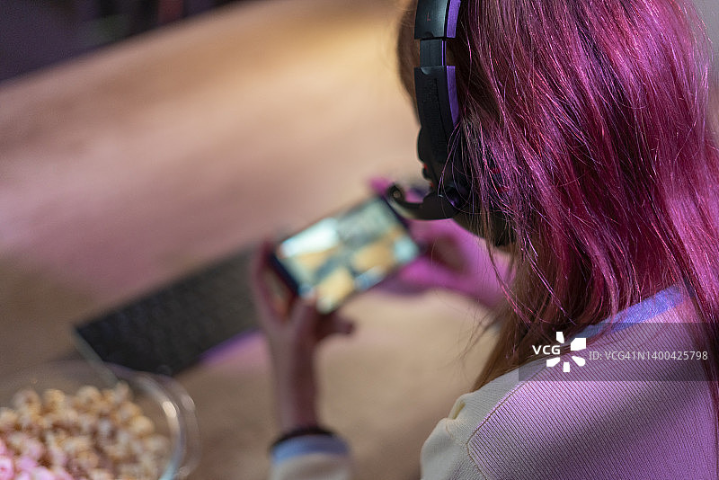 快乐女孩戴耳机用手机玩在线游戏图片素材