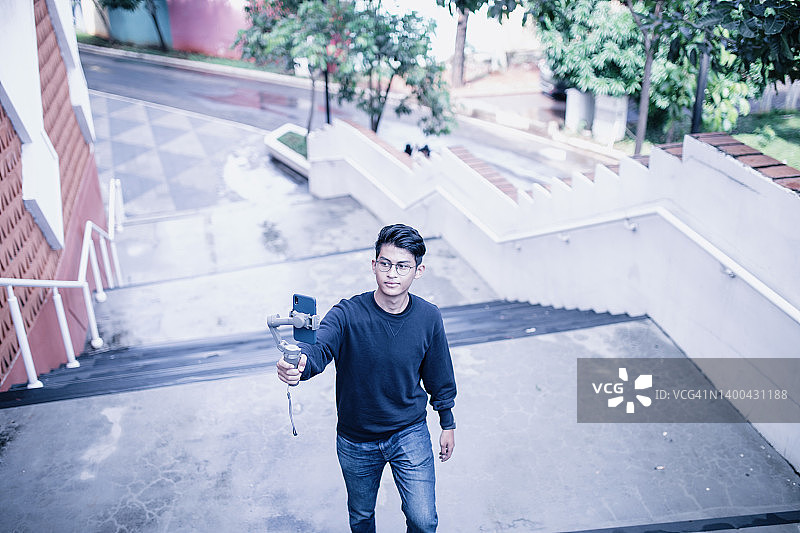 年轻的亚洲男子，视频博主，使用智能手机和云台拍摄视频图片素材