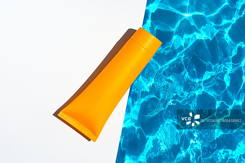 橙色软管包装的防晒霜、面霜或护手霜、沐浴露、洗发水，蓝色水池波浪背景图片素材