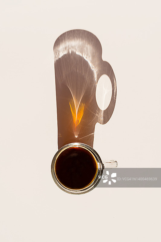 玻璃杯中的芳香早晨咖啡，米色背景上杯子的长阴影图片素材