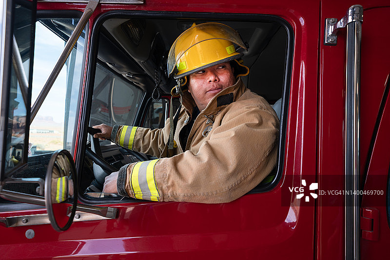 身穿全套防火装备在消防站的年轻消防员与消防车图片素材