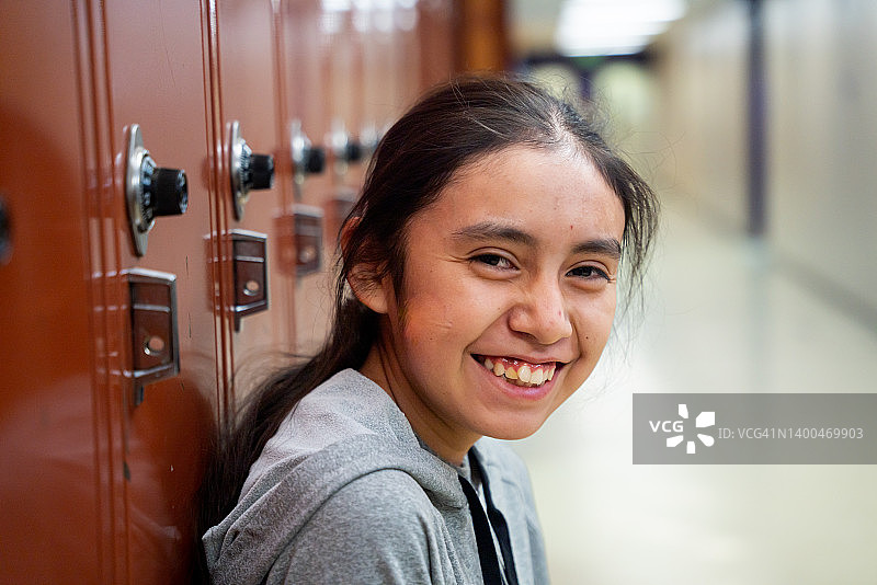 在学校走廊的储物柜旁，看向镜头的微笑高中少女肖像图片素材