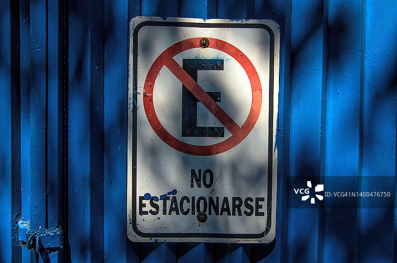 蓝色金属门上的西班牙语标志，声明“禁止停车”图片素材