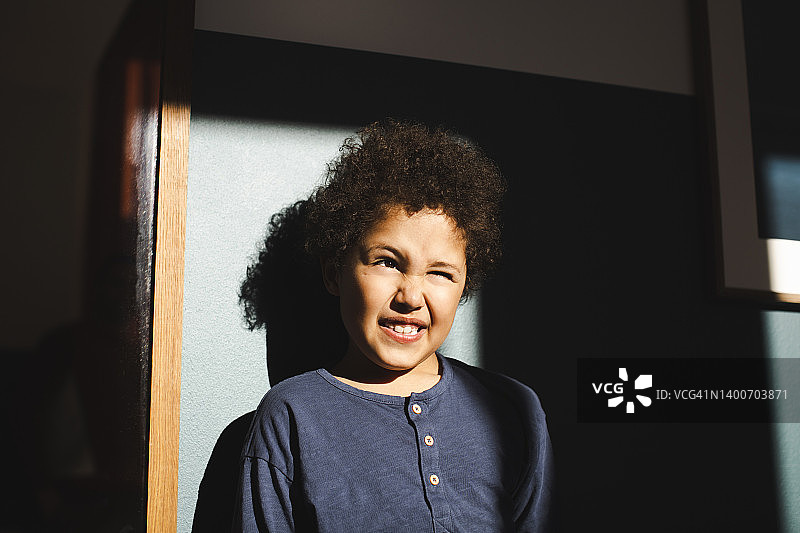 男孩站在阳光下靠着墙眨眼睛图片素材