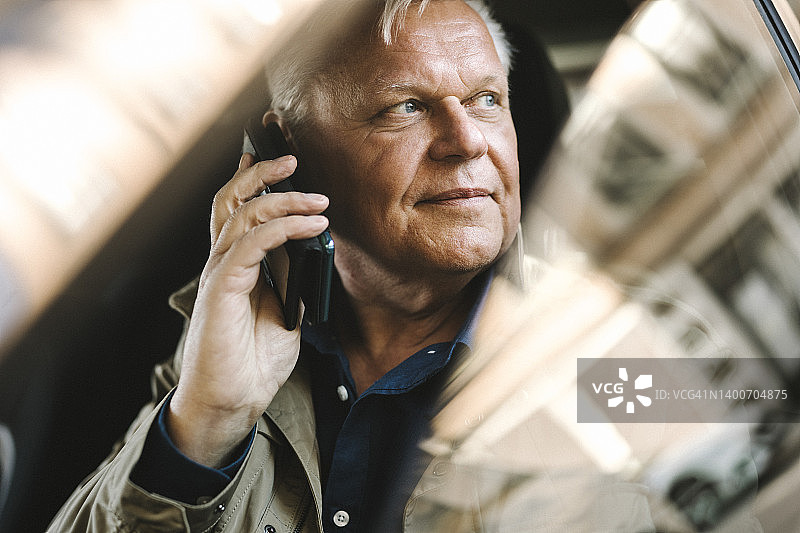 沉思的年长商人坐在车里用智能手机聊天图片素材