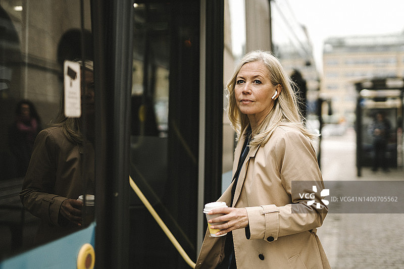 在城市里拿着一次性杯子登上公共汽车的商务女人图片素材