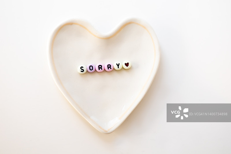 陶瓷心形盘子上用珠子写着“对不起”图片素材