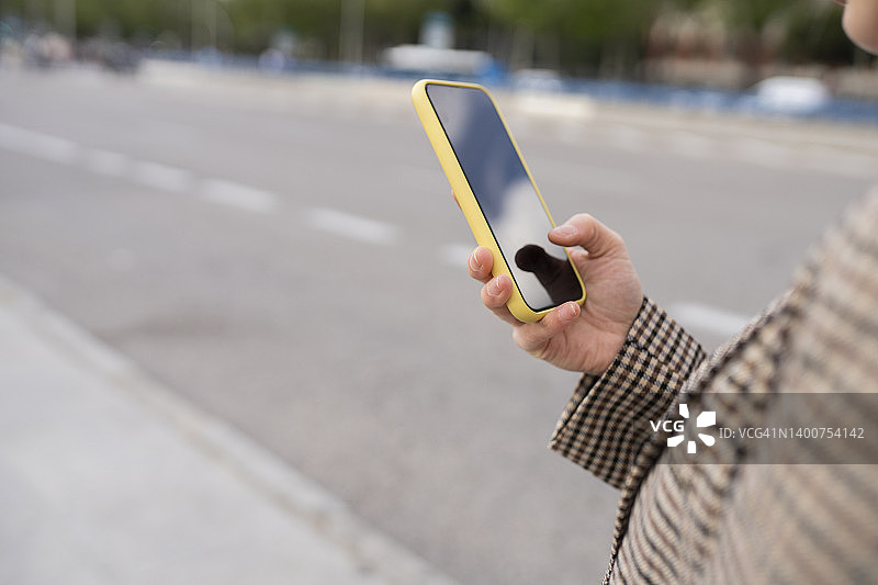 女人手持智能手机，背景是模糊的城市道路，互联网导航与现代科技概念图片素材