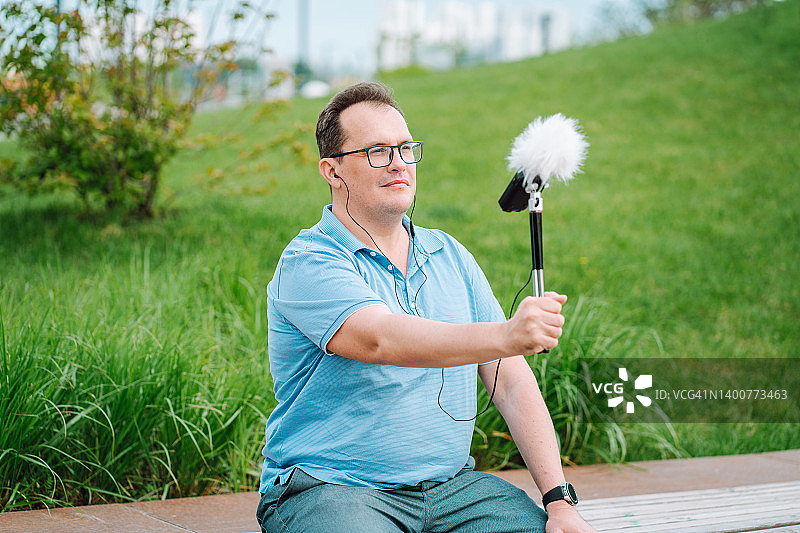 戴眼镜的成熟男人坐在公园长椅上，用麦克风测量噪音图片素材