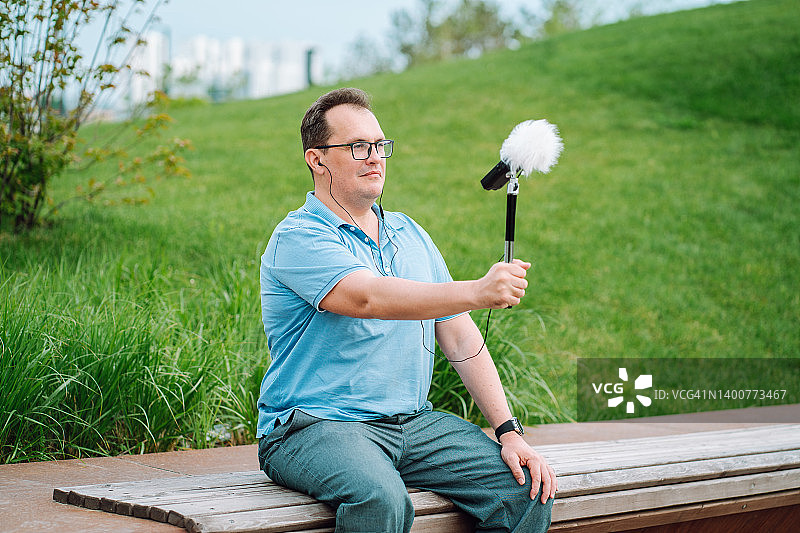 在公园长椅上用仪器测量噪声信号水平的中年男人图片素材