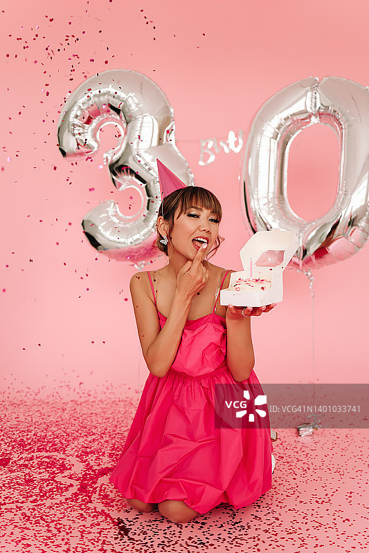 年轻女子身穿粉色迷你裙，在三十岁生日派对上手捧蛋糕庆祝图片素材