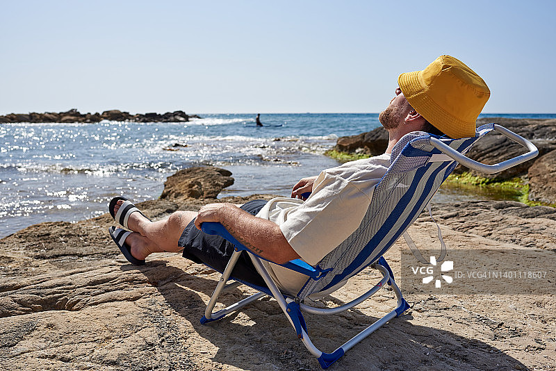 一位身份不明的男人在岩石海滩的户外椅上休息图片素材