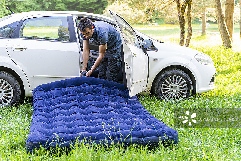 男子用连接到汽车的压缩机给行军床充气图片素材