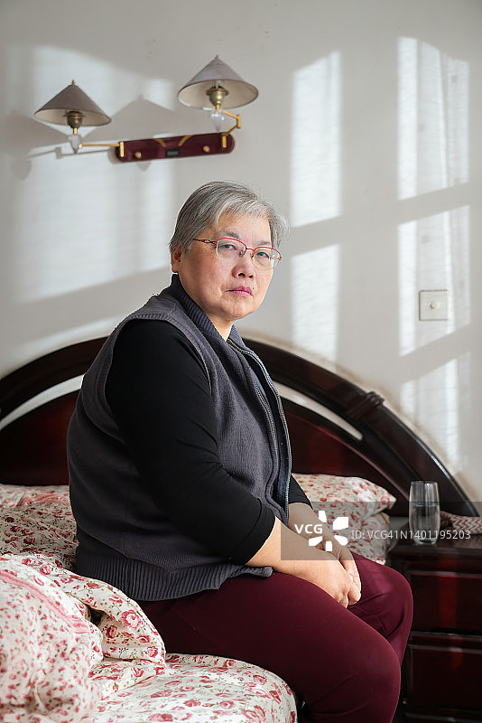 孤独的老妇人坐在床上看着镜头图片素材