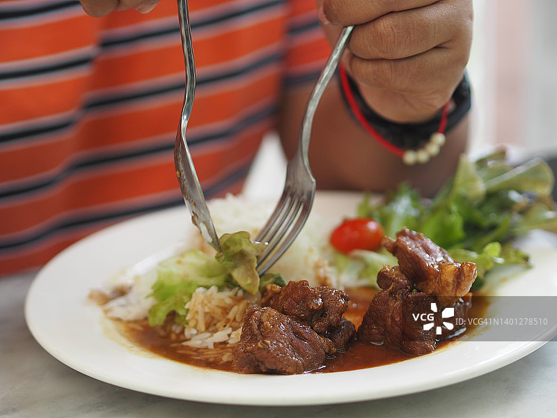 亚洲女人用刀叉在餐桌上吃白盘里的烤肉饭图片素材