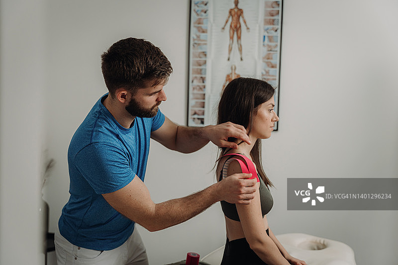 男理疗师在水疗沙龙为受伤女子肩部贴肌内效贴图片素材