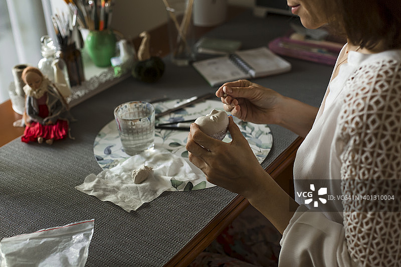 中年妇女在家里的桌旁雕刻娃娃脸图片素材
