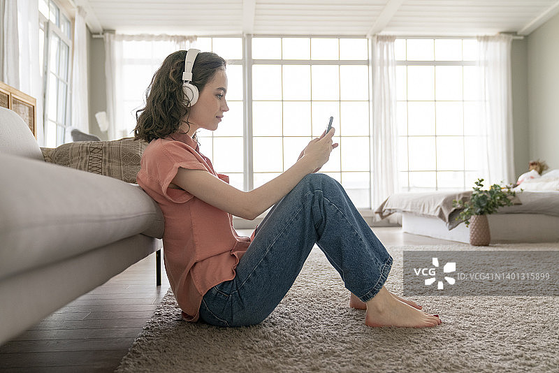 在家里坐在地毯上使用智能手机的年轻女人图片素材