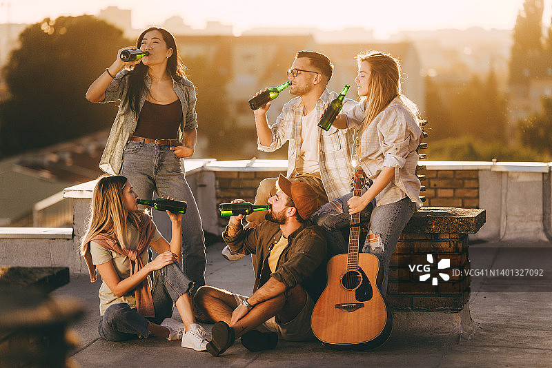 年轻朋友在屋顶日落时喝啤酒图片素材