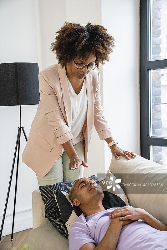 年轻的心理医生为躺在沙发上的病人进行催眠治疗图片素材