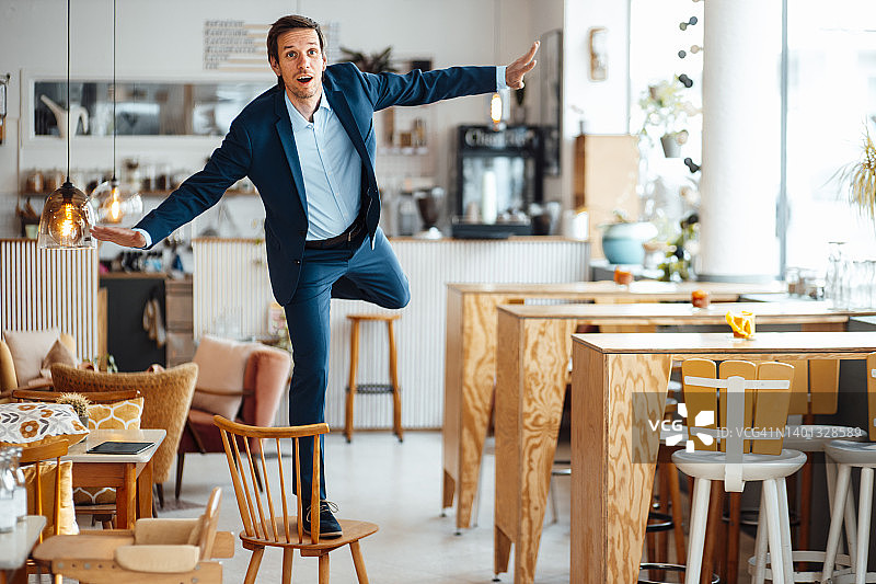 在咖啡馆站在椅子上伸出双臂的商人图片素材