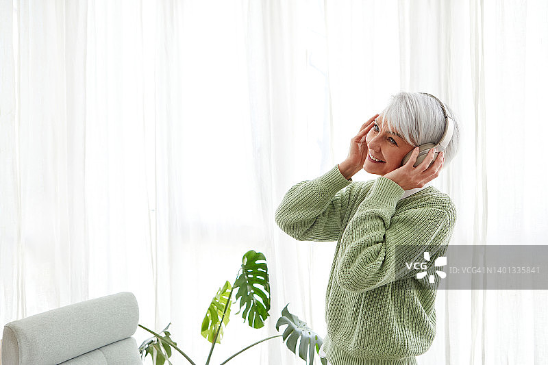 快乐的成熟女性戴着耳机听音乐，面带微笑图片素材