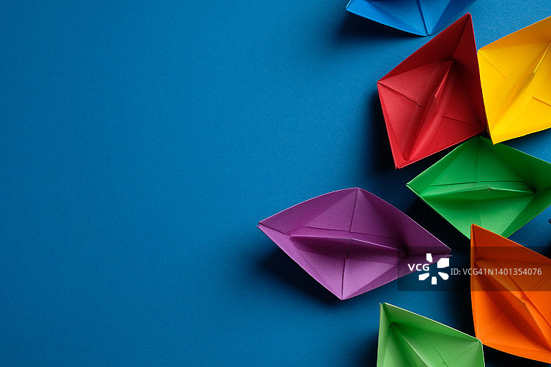蓝色背景上手工制作的彩色纸船，商业团队和领导力竞争概念，留白图片素材