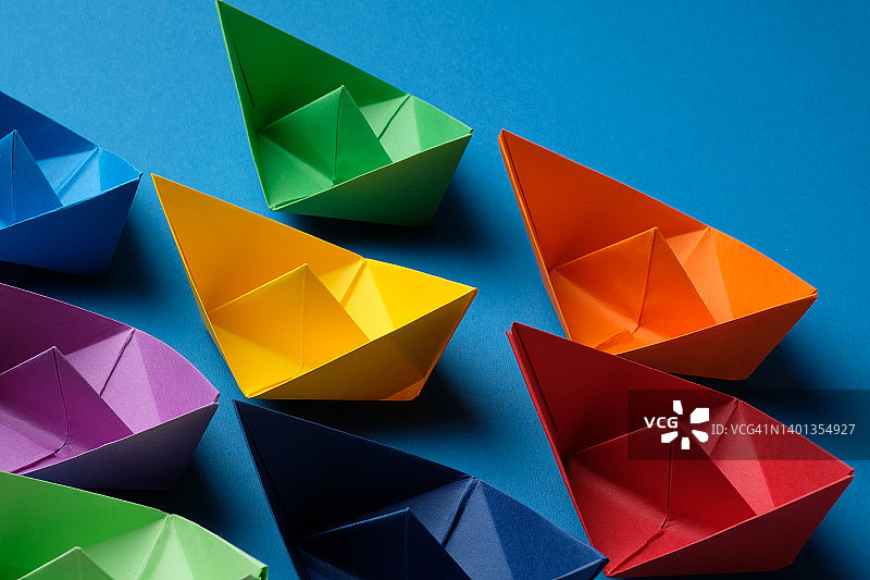 蓝色背景上手工制作的彩色纸船，商业团队和领导力竞争概念，留白图片素材