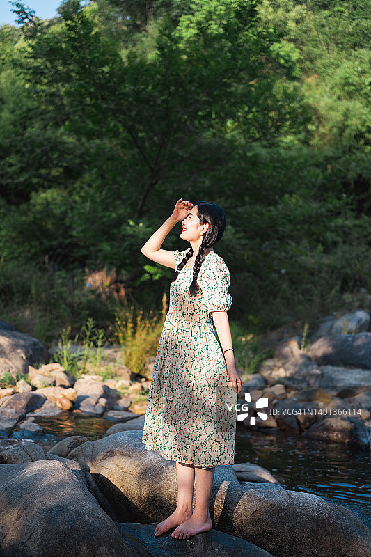 身穿长裙站在河边石头上的年轻亚洲女子全身照图片素材