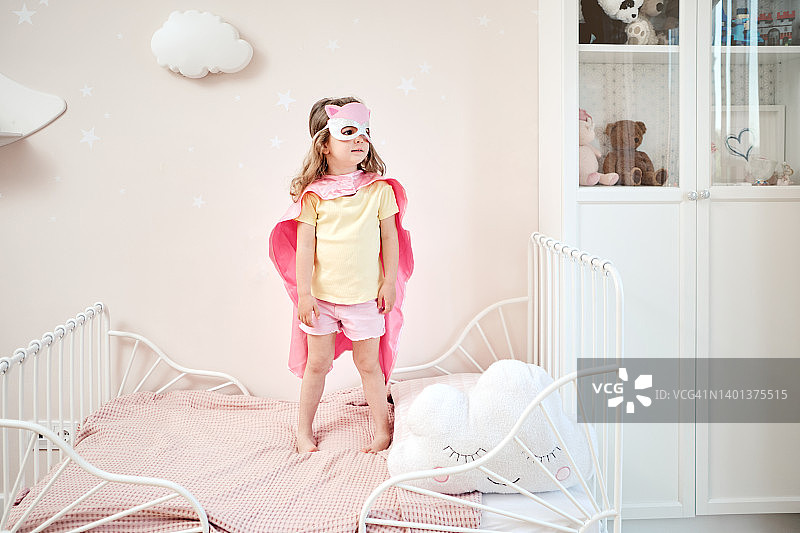 装扮成超级英雄的女孩在床上玩耍图片素材