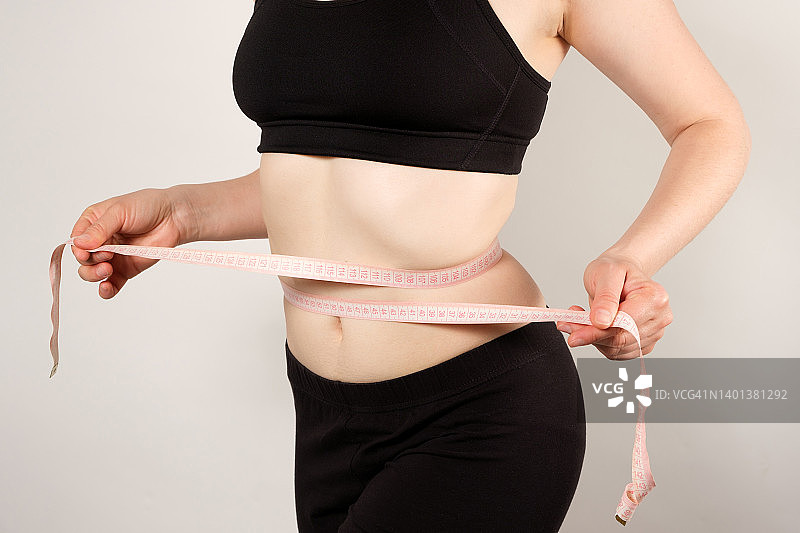一名妇女用厘米卷尺测量腹部周长特写，瘦身概念图片素材