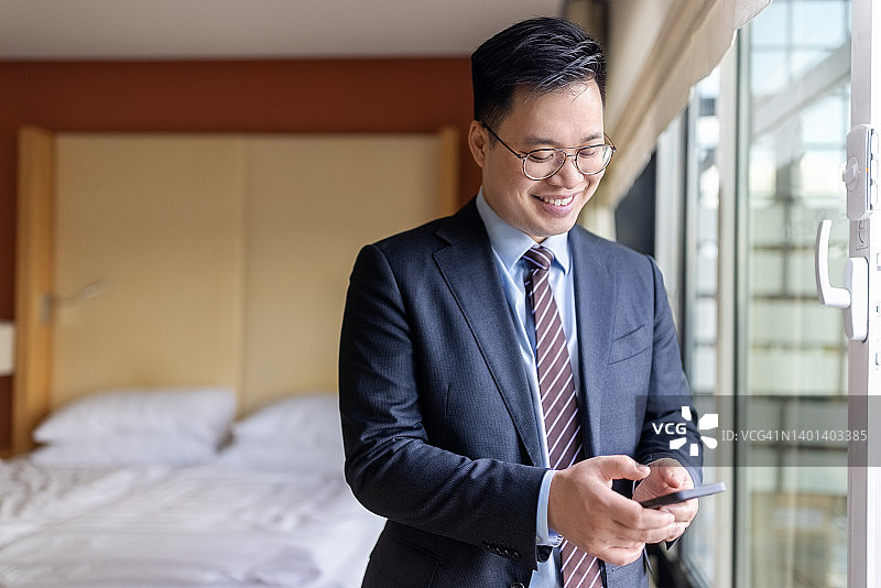 亚洲商人站在酒店房间里使用手机图片素材