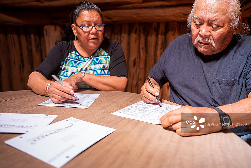 年长夫妇坐在他们的霍根小屋里，查看每位候选人，投票并签署选票图片素材