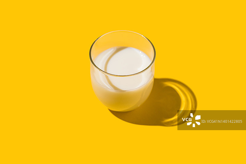 黄色背景硬光下的装满牛奶的玻璃杯，乳制品，短缺，钙，成长和饮用概念图片素材