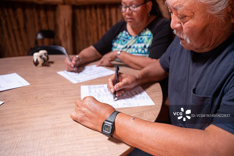 年长夫妇坐在他们的霍根小屋里，查看每位候选人，投票并签署选票图片素材