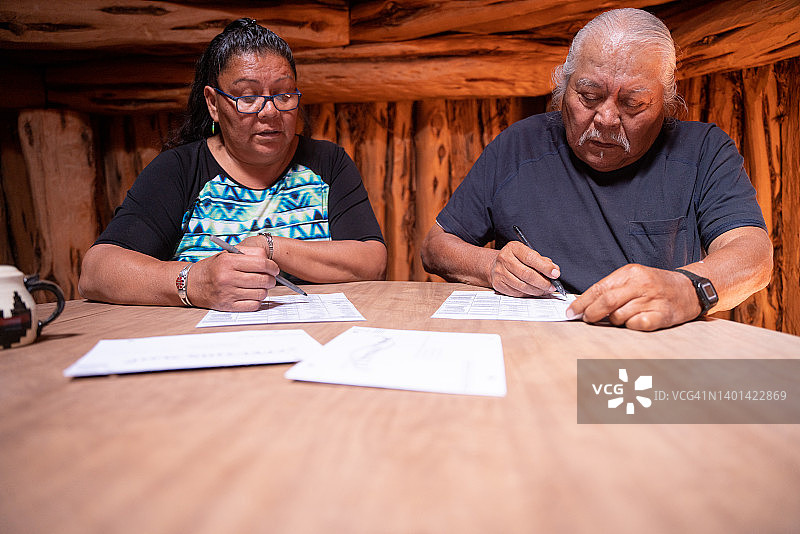 年长夫妇坐在他们的霍根小屋里，查看每位候选人，投票并签署选票图片素材