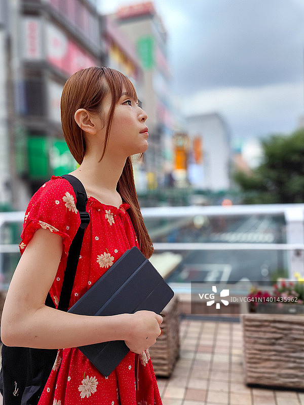 年轻女子携带平板电脑在城市中行走侧视图图片素材