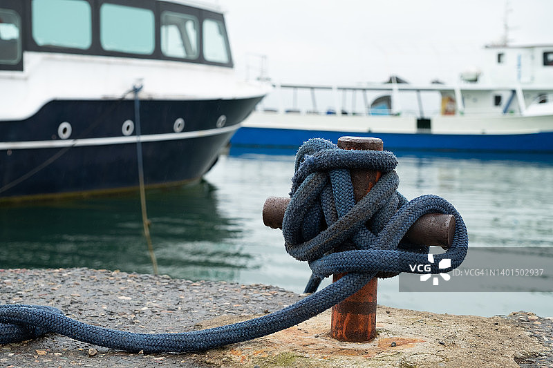 系船柱，带有系泊绳，安装在海边的混凝土泊位上，系泊缆绳用海结系在一起，在蔚蓝色大海附近的岸边图片素材