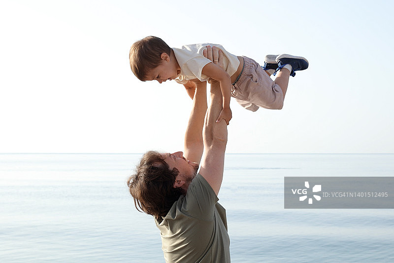 日落时分，年轻的父亲和儿子在海边玩耍，父亲节图片素材