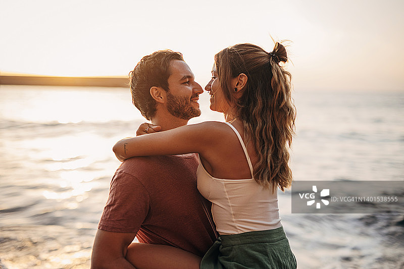 在海滩日落时拥抱的年轻夫妇图片素材