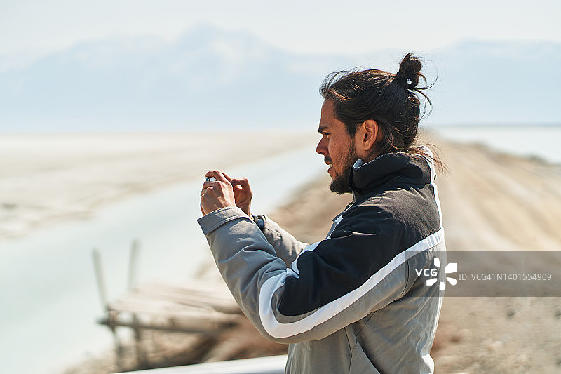 年轻的少数民族男游客拍摄盐湖岸边的风景图片素材