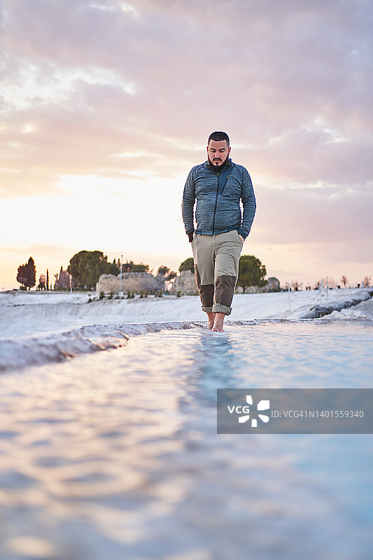 年轻男游客在日落天空下走在石灰华地貌上图片素材